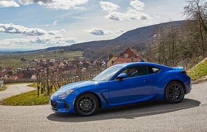 Der Subaru BRZ als blaues Sportcoupé auf kurviger Landstraße mit Dorf im Hintergrund