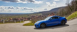 Der Subaru BRZ als blaues Sportcoupé auf kurviger Landstraße mit Dorf im Hintergrund