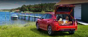 Roter Impreza mit offenen Kofferraum vor einem See im Sommer