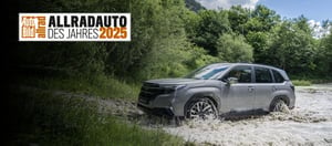 Auto Bild Allradauto des Jahres 2025 Badge und darunter ein Subaru Forester der gerade einen Fluss durchquert hat mit Wald im Hintergrund.