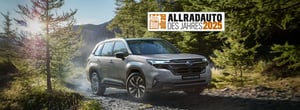 Subaru Forester fährt auf Waldweg mit Bäumen und Bergen im Hintergrund und Auszeichnung 'Allradauto des Jahres 2025'