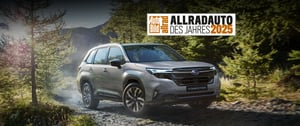 Subaru Forester auf Waldweg mit Bäumen und Bergen im Hintergrund und Auszeichnung 'Allradauto des Jahres 2025'