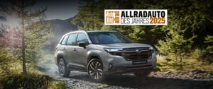 Subaru Forester auf Waldweg mit Bäumen und Bergen im Hintergrund und Auszeichnung 'Allradauto des Jahres 2025'