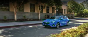 Blauer Subaru Impreza fährt auf einer Stadtstraße vor einem Gebäude mit Bäumen