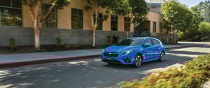 Blauer Subaru Impreza fährt auf einer Stadtstraße vor einem Gebäude mit Bäumen