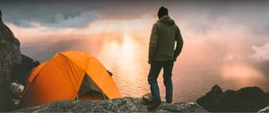 Person beim Campen an einer Küste mit orangenen Zelt bei Sonnenuntergang.