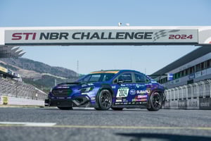 Blaue Subaru Rennwagen auf Rennstrecke unter Banner 'STI NBR CHALLENGE 2024' stehend