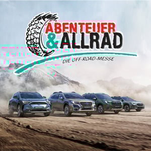 Vier Subaru SUVs fahren auf unbefestigtem Weg vor Bergkulisse mit Badge einer Offroad-Messe
