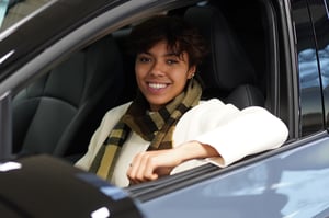 Junge Frau mit kurzem Haar und kariertem Schal sitzt lächelnd auf dem Fahrersitz eines Subarus