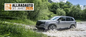Auto Bild Allradauto des Jahres 2025 Badge und darunter ein Subaru Forester der gerade einen Fluss durchquert hat mit Wald im Hintergrund.
