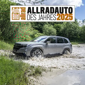 Auto Bild Allradauto des Jahres 2025 Badge und darunter ein Subaru Forester der gerade einen Fluss durchquert hat mit Wald im Hintergrund.