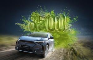 Subaru Solterra fährt auf Straße, dahinter große grüne Zahl '8.500€'